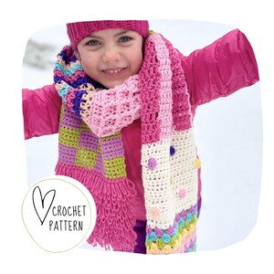 Pode incluir: Um conjunto de cachecol e chapéu de crochê coloridos, em tons de rosa, roxo, verde e creme. O cachecol apresenta um padrão xadrez, franjas e pompons. A imagem inclui o texto "Crochet Pattern" dentro de um coração.