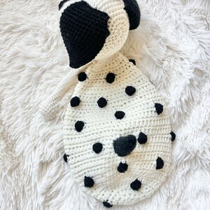May include: A white crocheted stuffed animal shaped like a Dalmatian dog with black spots. The dog has a black crocheted nose and ears.