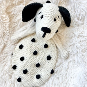 May include: White crocheted dog toy with black spots and ears. The toy is lying on a white fluffy surface.