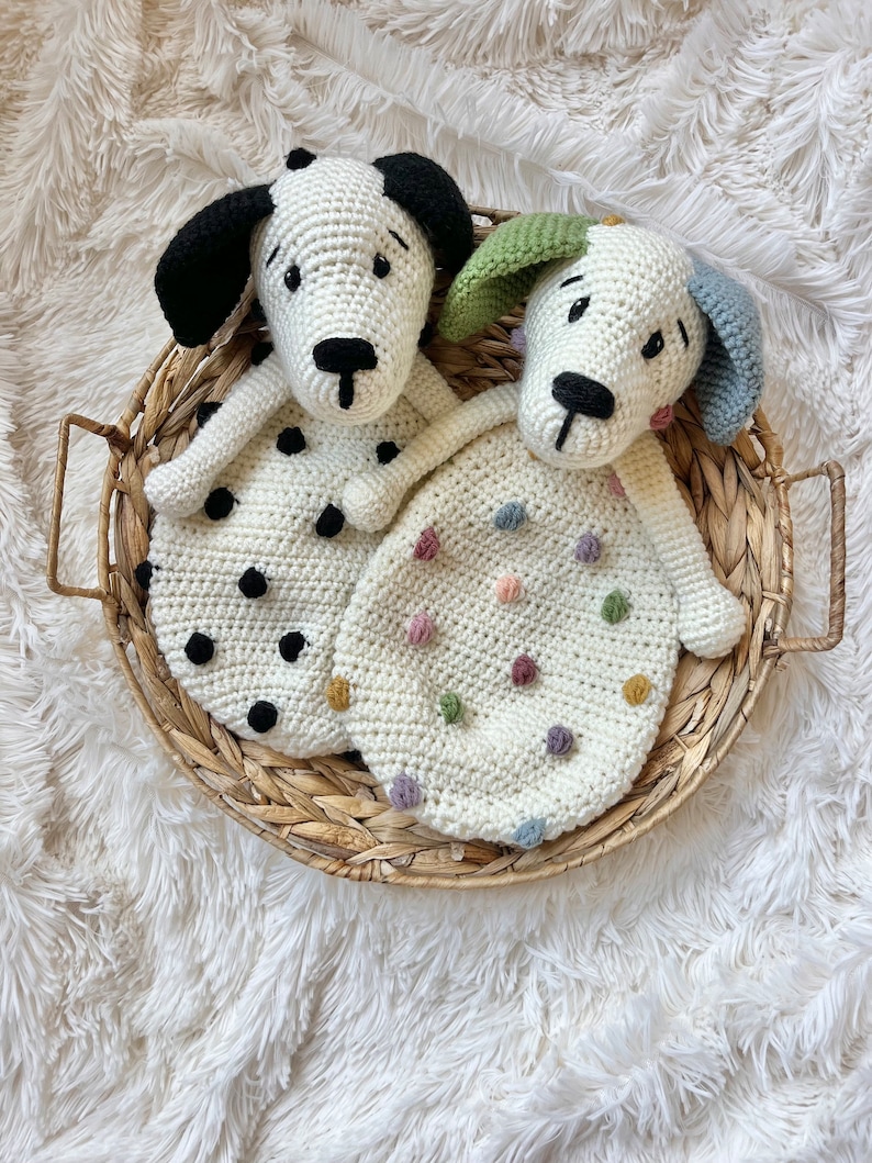 May include: Two crocheted dog-shaped baby blankets in a wicker basket. One blanket is white with colorful polka dots and the other is white with black polka dots.