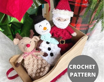 May include: A wooden sleigh filled with crocheted Christmas figures: a reindeer, a snowman, and Santa Claus. The reindeer is tan with a red nose and a pink bow. The snowman has a black hat and scarf. Santa wears a red suit.