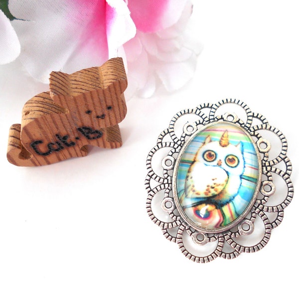 Broche ovale cabochon en verre hibou licorne blanc sur fond rayé multicolore