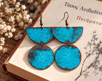 May include: A pair of drop earrings featuring a semi-circular top piece and a circular bottom piece, both finished in a vibrant turquoise blue with dark brown, oxidised metal edges. The earrings hang from simple bronze-toned metal hooks.