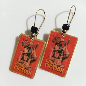May include: A pair of gold-toned earrings with black beads and rectangular red and gold charms. The charms feature a woman with black hair and a red dress, and the text "I said God Damn" and "Pulp Fiction".