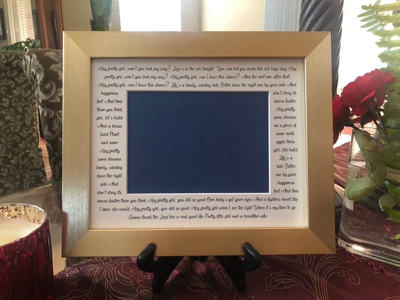 Op de afbeelding: Een gouden fotolijst met een blauwe passe-partout en een witte achtergrond. De lijst bevat een handgeschreven gedicht met de tekst "My pretty girl, won't you look my way?" en "And the next one after that..."