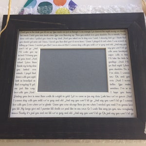 May include: A black picture frame with a white mat and a printed lyric from a love song. The lyrics are about a couple's love and commitment to each other. The frame has a space for a photo in the center.