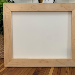 May include: A natural wood picture frame with a light wood finish. The frame is empty and ready to display a photo or artwork.