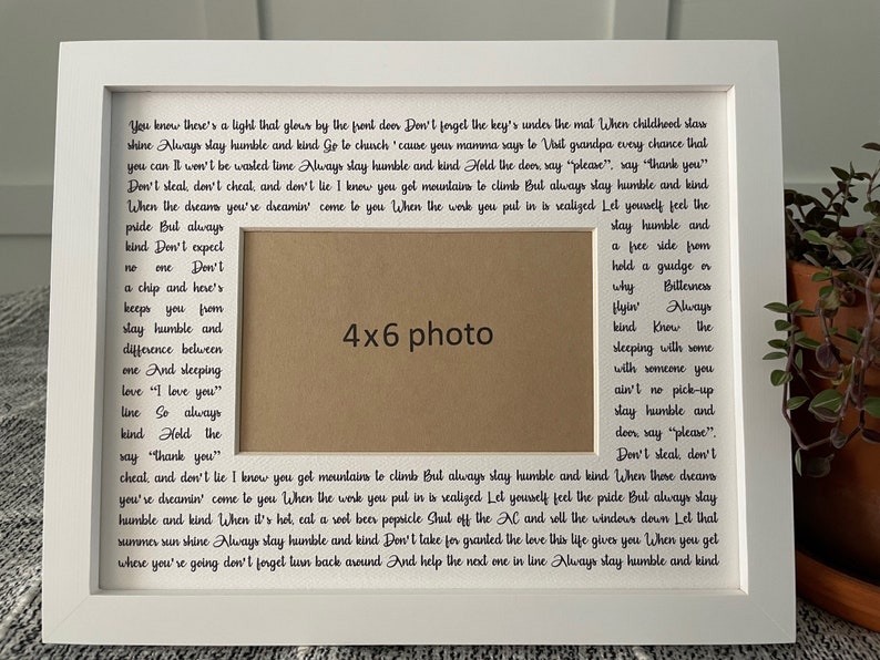 Op de afbeelding: Een wit fotolijstje met een fotoopening van 10,2 x 15,2 cm. De lijst heeft een witte passe-partout en een zwarte inscriptie die luidt: "You know there's a light that glows by the front door Don't forget the key's under the mat When childhood slaw shine Always stay humble and kind Go to chuch 'cause your mamma says to Vail grandpa every chance that you can Il won't be wealed time Always slay humble and kind Hold the deer say "please", say "thank you" Don't steal, don't cheal, and dew't lie I know you get mountains le climb Bul always slay humble and kind When the dreams you're dreamin' come to you When the work you pul in is realized Let youself feel the pride But always kind Don't expect one Don't stay humble and a pee side from hold a grudge or a chip and here's why Billeuses keeps you from stay humble and difference belween one And sleeping love "I love you" line So always kind Hold the say "thank you" cheal and don't lie I know you get mountains le climb Bul always stay humble and kind When those dreams you're dreamin' come to you When the work you pul in is realized Lel yourself feel the pride Bul always slay humble and kind When it's hol, cal a wel beer popsicle Shul off the M and roll the windows down Lel thal summer sun shine Always slay humble and kind Don't take for granted the love this life gives you When you gel where you're going don't forget turn back around And help the ned one in line Always stay humble and kind"