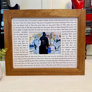 May include: Wooden framed print featuring a family photo with Star Wars characters Darth Vader and Stormtroopers. The frame surrounds a printed hymn with the lyrics in a serif font.