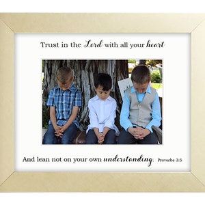 May include: A framed print with a gold frame and a white background. The print features a photo of three young boys sitting on a bench with their hands clasped in prayer. The text on the print reads "Trust in the Lord with all your heart and lean not on your own understanding. Proverbs 3:5."