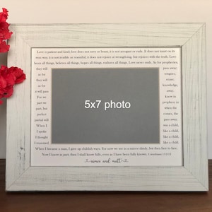 May include: A white wooden picture frame with a 5x7 inch photo opening. The frame has a distressed white finish and features a quote about love from the Bible, 1 Corinthians 13:12. The quote reads, "Love is patient and kind; love does not envy or boast, it is not arrogant or rude. It does not insist on its own way; it is not irritable or resentful; it does not rejoice at wrongdoing, but rejoices with the truth. Love bears all things, believes all things, hopes all things, endures all things. Love never ends. As for prophecies, they will pass away; tongues, knowledge, prophecy will pass away. When I was a child, I spoke like a child, I thought like a child, I reasoned like a child. When I became a man, I gave up childish ways. For now we see in a mirror dimly, but then face to face. Now I know in part; then I shall know fully, even as I have been fully known. Corinthians 13:12." The frame also includes the names "aimee and matt" written in cursive.
