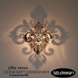 Puede incluir: Una l&aacute;mpara de pared de color dorado con un acabado de espejo y un dise&ntilde;o floral. La l&aacute;mpara proyecta una sombra en la pared detr&aacute;s de ella. El texto "Effet Miroir CONCEPT DESIGNER by Lyssandre Saint York bo-design. CONCEPT" es visible en la parte inferior de la imagen.