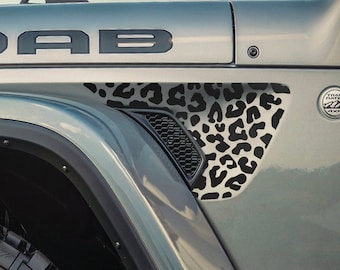 May include: Close-up of a gray Jeep with the word "MOAB" in black lettering. A black and white leopard print design is on the side panel. The tire is black with a black rim.