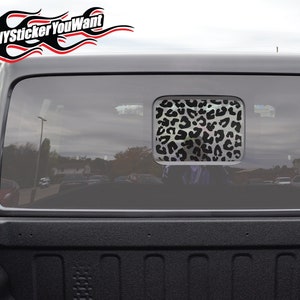 May include: Black and white leopard print decal on the rear window of a black pickup truck. The decal is in the shape of a square and is centred on the window. The truck is parked in a car park.
