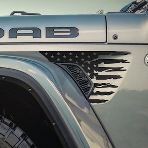 May include: A gray Jeep Wrangler with a black "MOAB" decal on the hood and a black and white American flag decal on the fender.