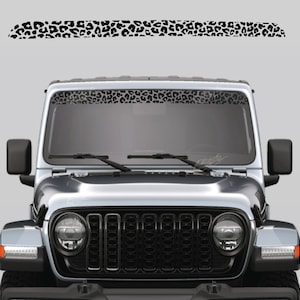 May include: A silver Jeep Wrangler with a black leopard print decal on the windscreen. The decal is a thin strip that runs across the top of the windscreen.