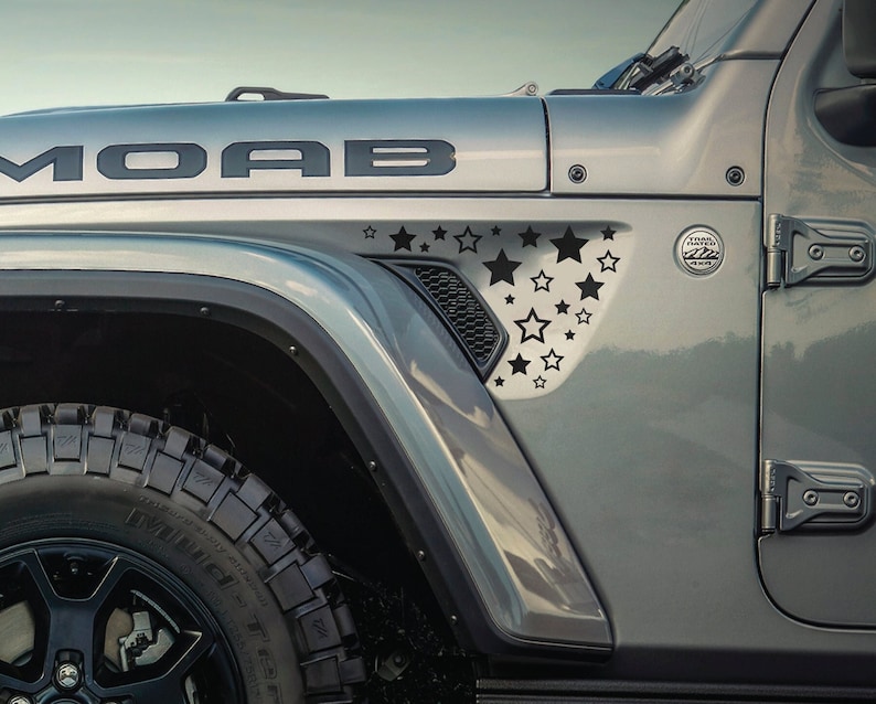 May include: A gray Jeep Wrangler with a black "MOAB" decal on the hood. The fender has a black star design decal.