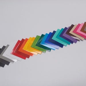 May include: A collection of colorful square samples arranged diagonally across a white surface. The samples display a range of colors, including black, gray, red, orange, yellow, green, blue, teal, purple, pink, and brown.