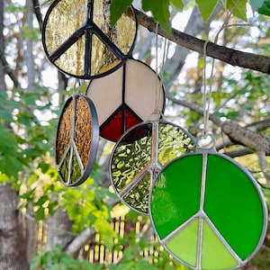 May include: Four stained glass peace sign ornaments hanging from a tree branch. The ornaments are in various colors, including gold, white, red, green, and brown.