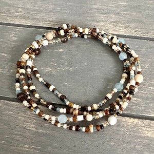 May include: A multi-strand beaded necklace with brown, white, and light blue beads. The necklace is made of various materials, including wood, glass, and metal.