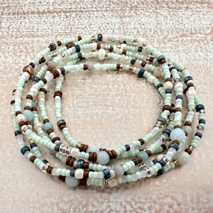 May include: A multi-strand beaded necklace with a mix of light blue, brown, white, and gray beads. The necklace is made of small, round beads and is wrapped around itself to form a circle.