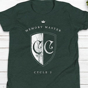 May include: A dark green t-shirt with a white crest featuring the letters "CC" and the text "MEMORY MASTER CYCLE 2" and the social media handle "@kadelmuldesigns".