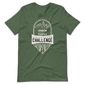 K&ouml;nnte beinhalten: Gr&uuml;nes T-Shirt mit einem wei&szlig;en Grafikdesign, das eine Bergkette und den Text "Laid my foundation, added the essentials, Rising to the challenge" zeigt. Die Grafik ist von einem Kreis mit dem Text "Discipline, Freedom, Choices, Consequences, Resilience" umgeben. Der Text "@kdelmuldesigns" befindet sich am unteren Rand des Shirts.