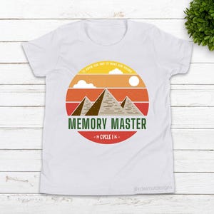 May include: White t-shirt featuring a retro-style graphic of three pyramids in front of a sunset with the text "Memory Master - Cycle 1 is -"