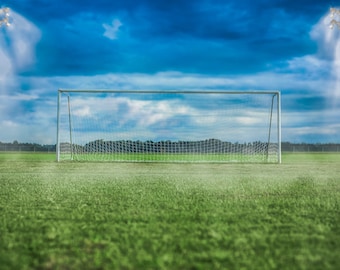 Puede incluir: Una portería de fútbol en un campo verde con un cielo azul y nubes blancas. Dos postes altos con luces están a cada lado de la portería.