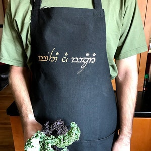 May include: A black apron with adjustable straps and a large pocket. The apron has the text "Mithril" written in Elvish script in gold.