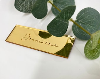 May include: Gold mirrored acrylic place card with the name "Jermaine" engraved in cursive script.