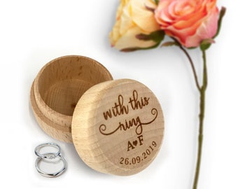 May include: A wooden ring box with the inscription "with this ring A♥F 26.09.2019". The box is open and two silver rings are inside.