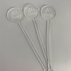 May include: Three clear acrylic drink stirrers with round tops. Each top has the text "Let's Party" written in white.