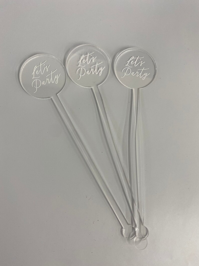 May include: Three clear acrylic drink stirrers with round tops. Each top has the text "Let's Party" written in white.
