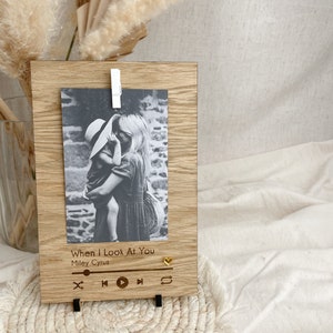 May include: A wooden photo frame with a black and white photo of a woman and child. The frame has a music player design with the text "When I Look At You" and "Miley Cyrus" engraved on it.