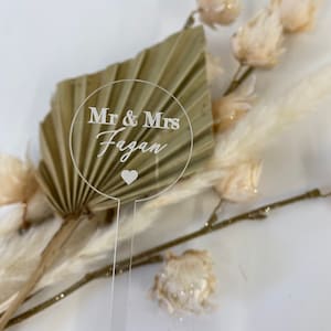 May include: A clear acrylic wedding sign with the text "Mr & Mrs Fagan" and a small heart.