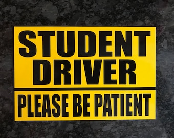 May include: Yellow sign with black text that reads "STUDENT DRIVER PLEASE BE PATIENT".