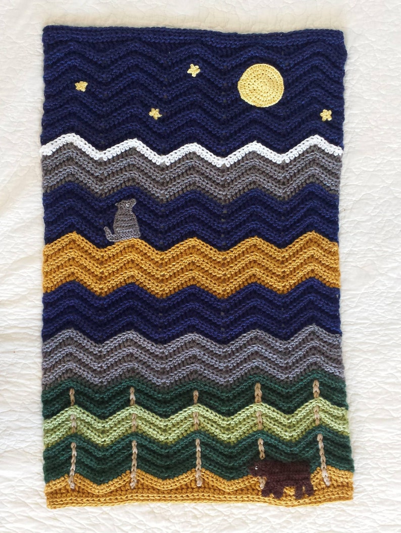 May include: Crocheted baby blanket with a blue, gray, green, and yellow chevron pattern. The blanket features a crocheted moon, stars, a bear, and a dog.