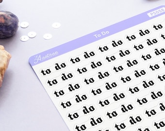 May include: A sheet of white stickers with the words "to do" printed in black gothic font. The stickers are arranged in rows and columns on a purple surface.