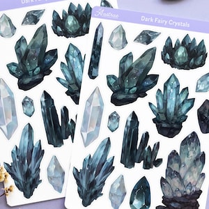 May include: Two sticker sheets with dark blue and teal crystal illustrations, labeled "Dark Fairy Crystals". The image also includes tarot cards, a candle, a crescent moon, a sun charm, and crystals on a lavender surface.