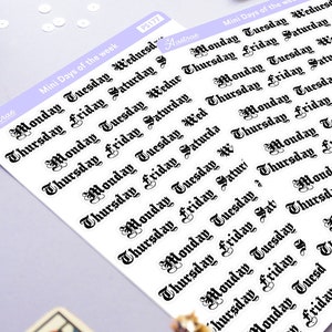 Puede incluir: Dos hojas de pegatinas con los días de la semana en fuente gótica. Las pegatinas son blancas con texto negro y un borde morado claro. También se ve una carta del tarot, una luna creciente y un sol.