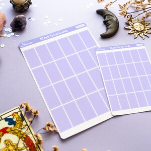 May include: Two lavender-colored blank tarot card sheets with grid layouts, labeled "Blank Tarot Cards" and "Aastrae". A vintage tarot card, a bronze moon, and a sun charm are also visible. The background is a light purple.