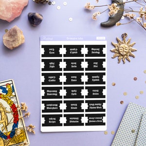 May include: A sheet of black and white stickers with gothic font text. The stickers are labeled with various topics related to witchcraft, such as tarot, crystals, astrology, sigils, herbs, altar, candles, runes, symbols, numerology, spells, deities, moon phases, rituals, shadow work, recipes, divination, and potions and brews.