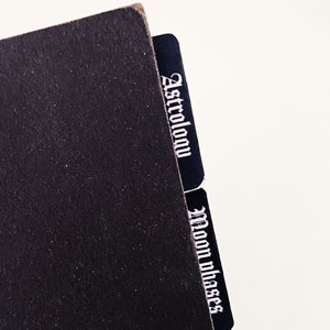 May include: Black notebook with two black index tabs labeled "Astrology" and "Moon Phases".