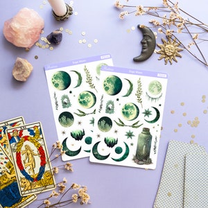 Puede incluir: Dos hojas de pegatinas con tem&aacute;tica de luna de salvia con ilustraciones verdes y blancas de lunas, estrellas y plantas. Las pegatinas est&aacute;n sobre un fondo morado claro con otros art&iacute;culos decorativos.