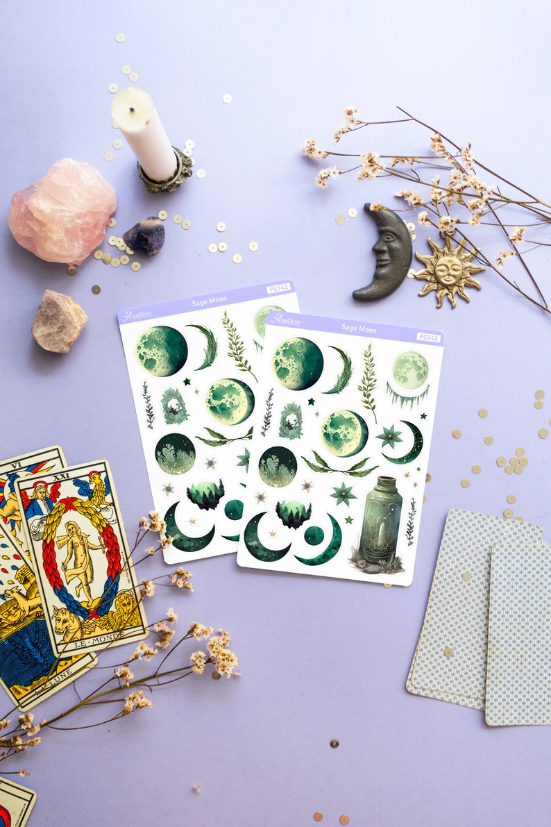 Puede incluir: Dos hojas de pegatinas con tem&aacute;tica de luna de salvia con ilustraciones verdes y blancas de lunas, estrellas y plantas. Las pegatinas est&aacute;n sobre un fondo morado claro con otros art&iacute;culos decorativos.