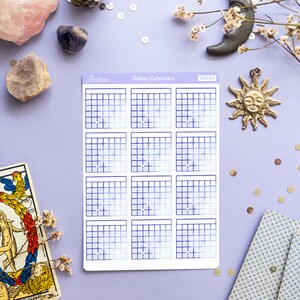 Op de afbeelding: Een vel met galaxy-kalender stickers met een blauw en wit verloop. De stickers zijn gerangschikt in een raster van 12, waarbij elke sticker een andere kalendermaand voorstelt. De stickers zijn gelabeld met "Galaxy Calendars" en "PS263".