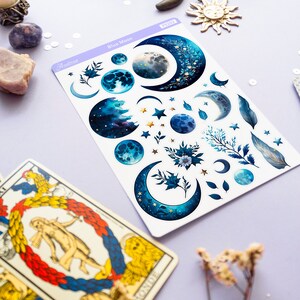 May include: A sheet of blue moon themed stickers with crescent moons, stars, and floral designs. The stickers are on a white background and have a light blue border. The text "Astro" and "Blue Moon" are printed on the sheet.