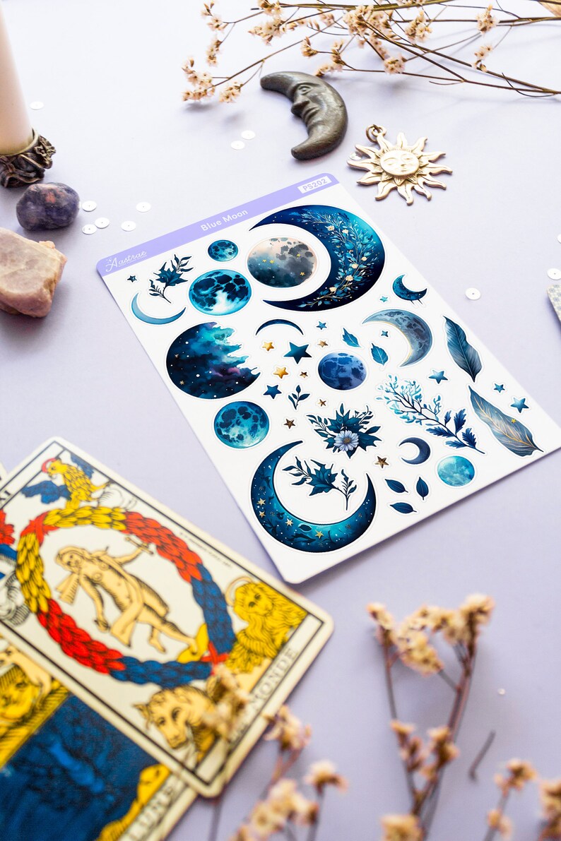May include: A sheet of blue moon themed stickers with crescent moons, stars, and floral designs. The stickers are on a white background and have a light blue border. The text "Astro" and "Blue Moon" are printed on the sheet.