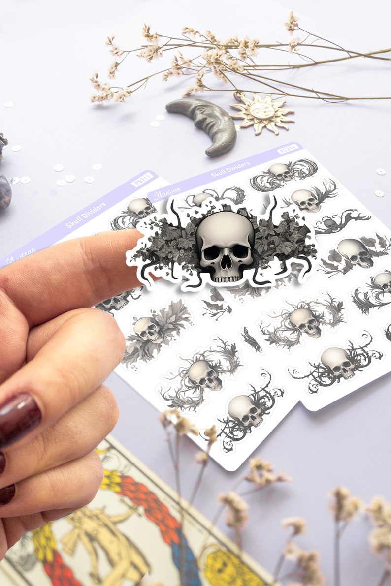 May include: A sheet of skull divider stickers with a large skull surrounded by black and white floral designs. The sheet also includes smaller skulls with floral designs.